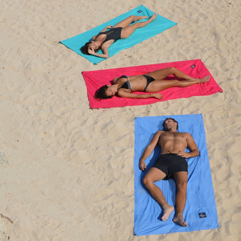 Drap de plage SOLO en version turquoise, framboise et bleu d'Ôbaba - personnes allongées sur le sable